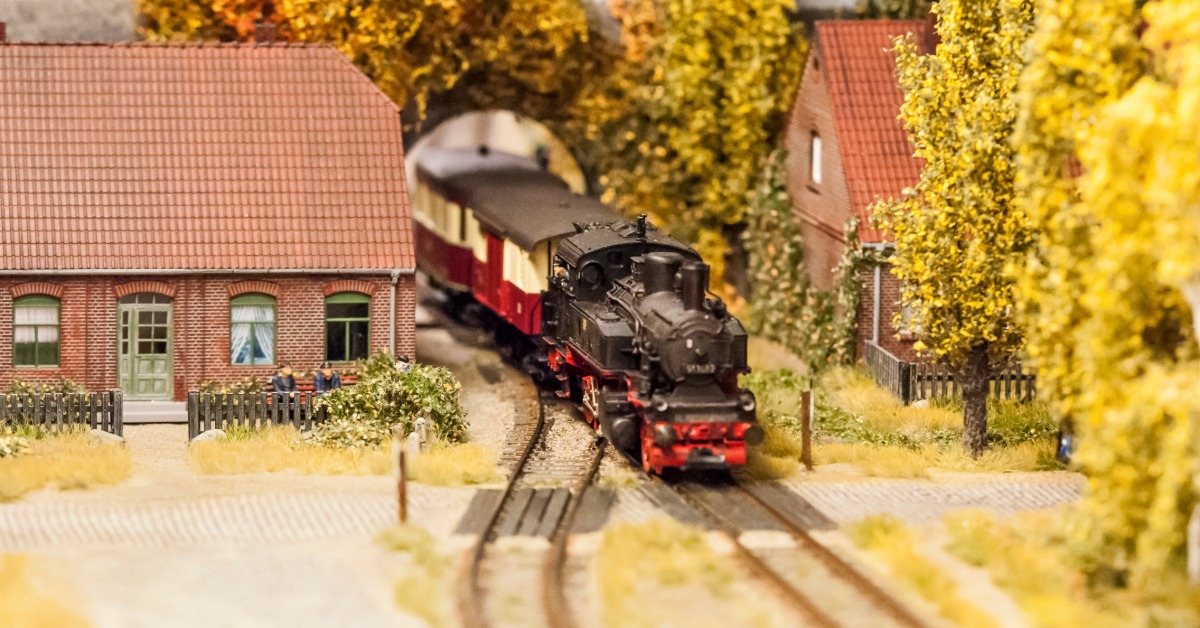 A model railway with a small steam train coming through an overpass. There are model trees all around the track.