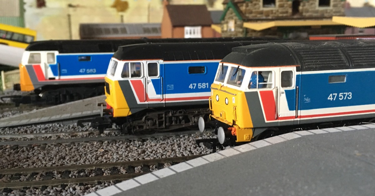 Three blue model trains parked on parallel tracks to each other. They are pulled into a model train station.