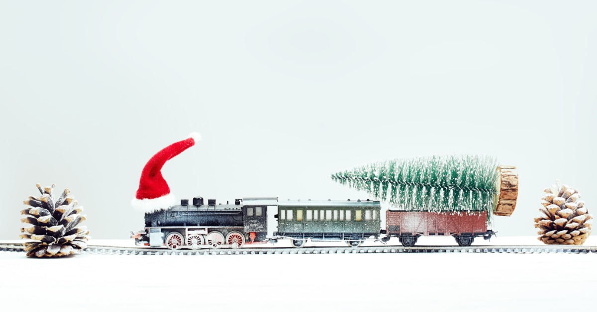 A Christmas toy train running along a small section of track. The train is transporting a white Christmas tree.