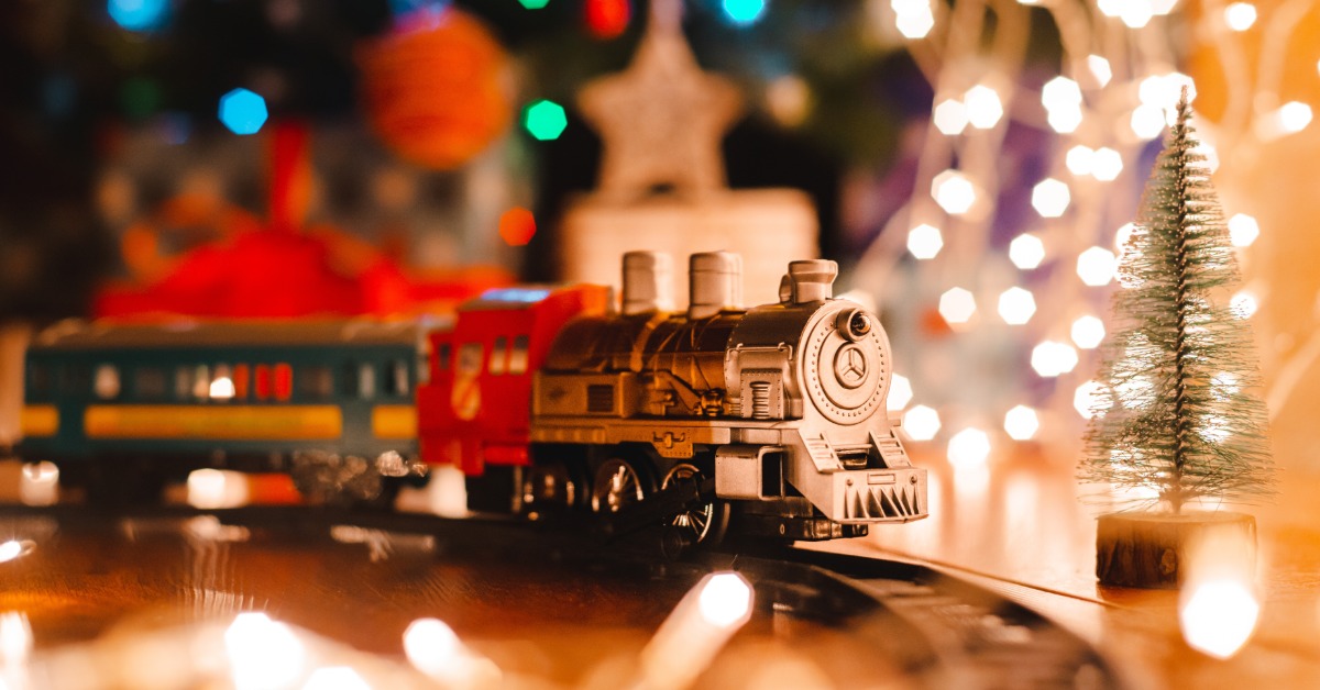 A vintage toy steam train on a toy train track. There are bright Christmas lights placed behind the track.