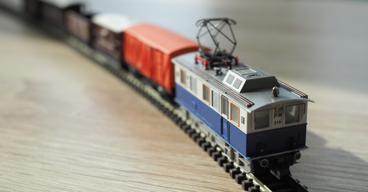 An N-scale model train on a small track that is placed on a wooden table. The train is six cars long.