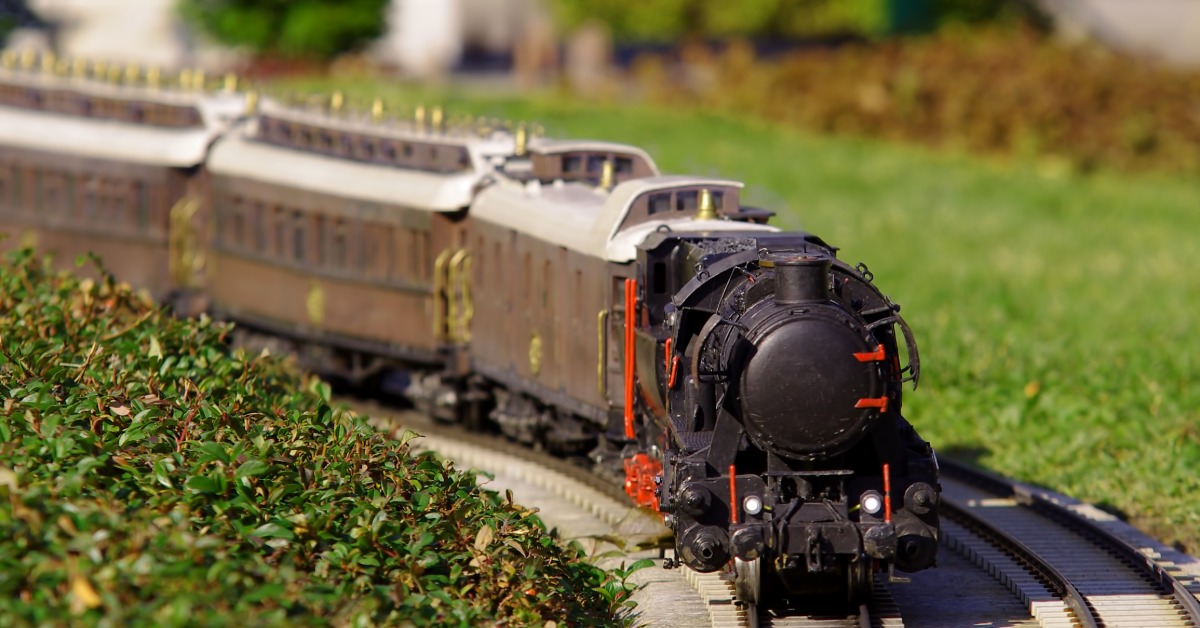 A closeup on a small, black, model train operating along a railway. The track is positioned next to a patch of grass.