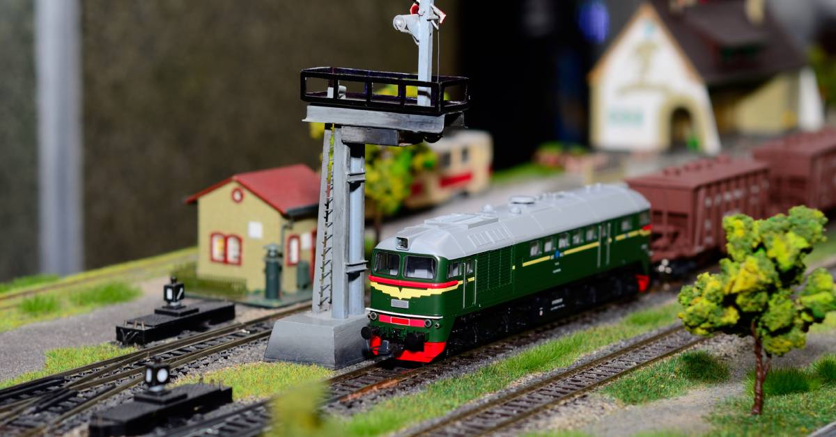 A close-up of a model train on a railway. Around the train there are lots of details like grass and trees.