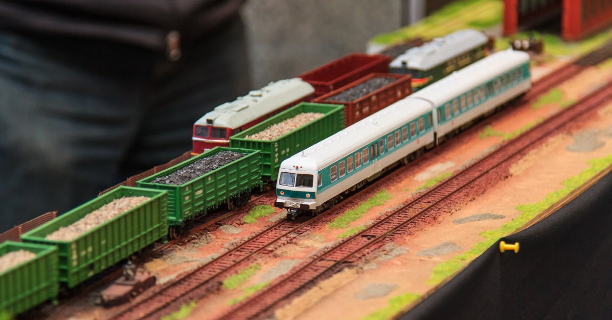 A few different model train cars are sitting on a railroad track. A person is standing behind the models.