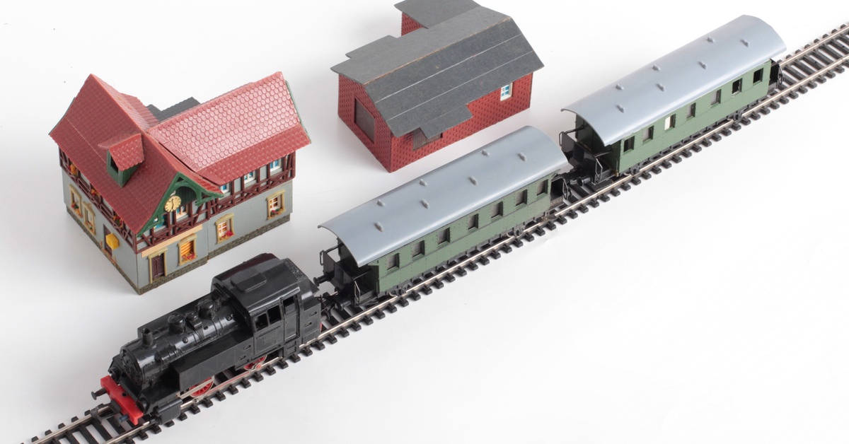 A small model trainset is going down the train track. Small model houses are next to the tracks.