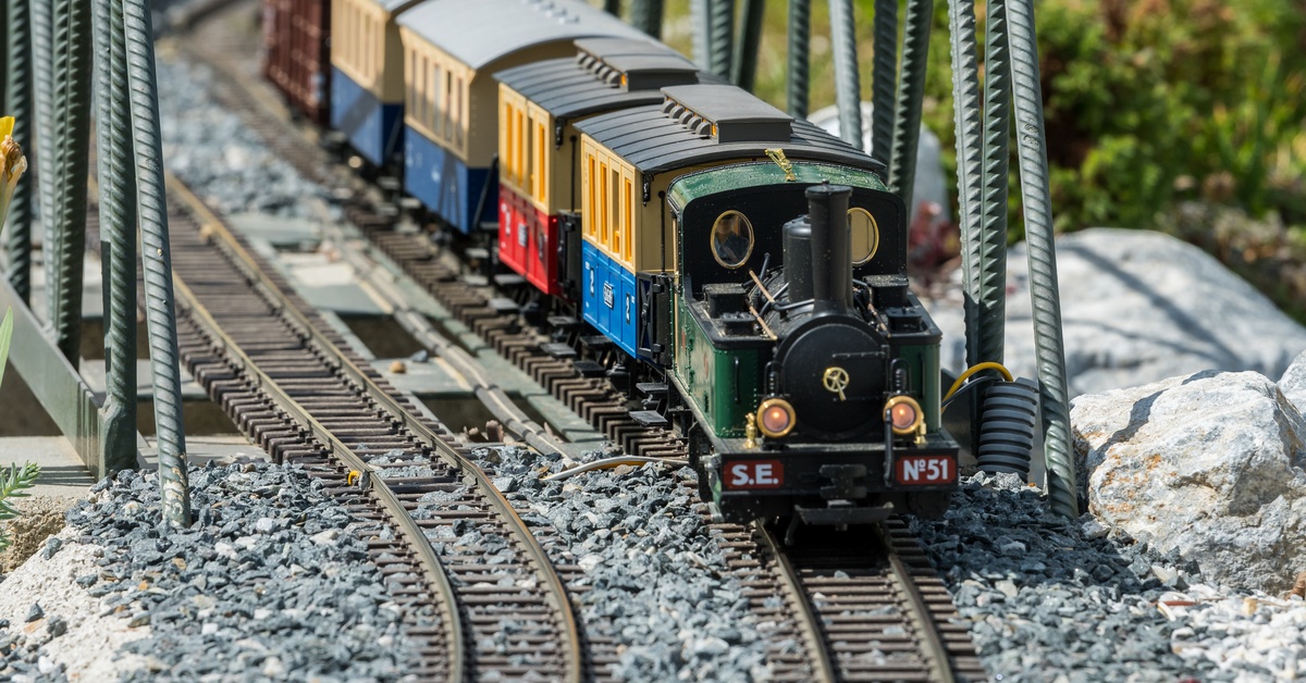 A model train sitting on a train track across a bridge. The track is decorated with small gravel and rocks.