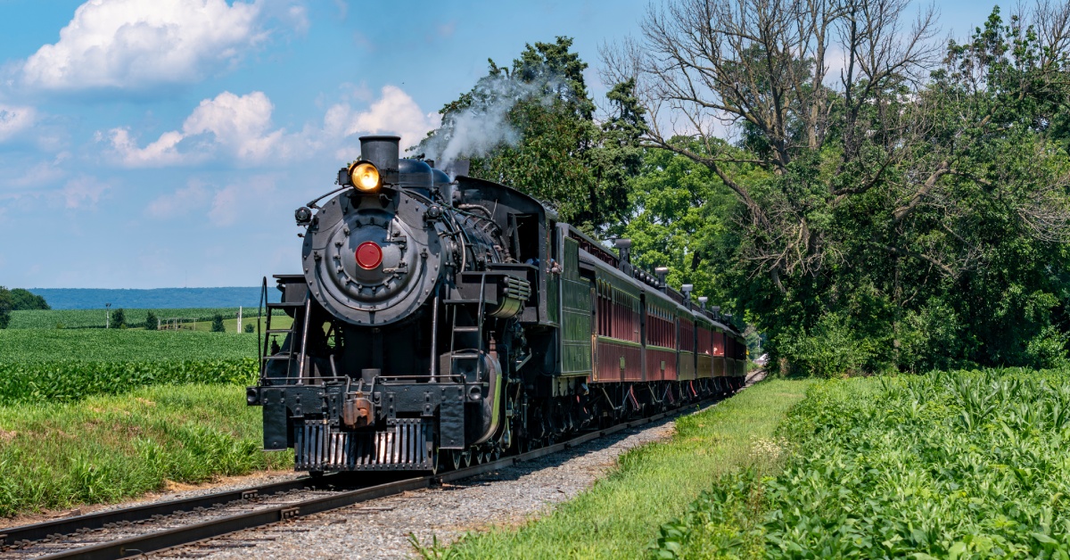A steel passenger train driving through an empty landscape while some smoke comes out from the top of the train.