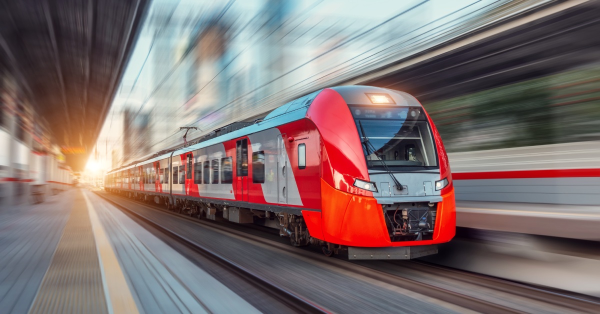 A modern and sleek passenger train driving through a train station. It's going very fast so there is a motion blur behind it.
