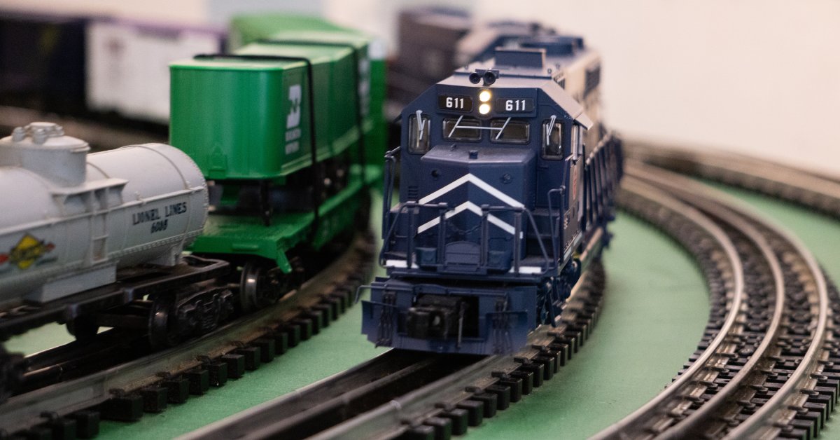 A close up of a model railroad with three curved tracks. A blue train is cruising around the curve in the middle track.
