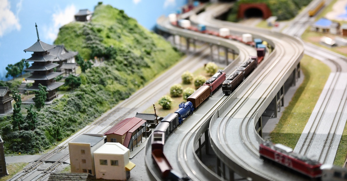 A model train set drives through a model of rural Japan with small buildings, greenery, and a temple.