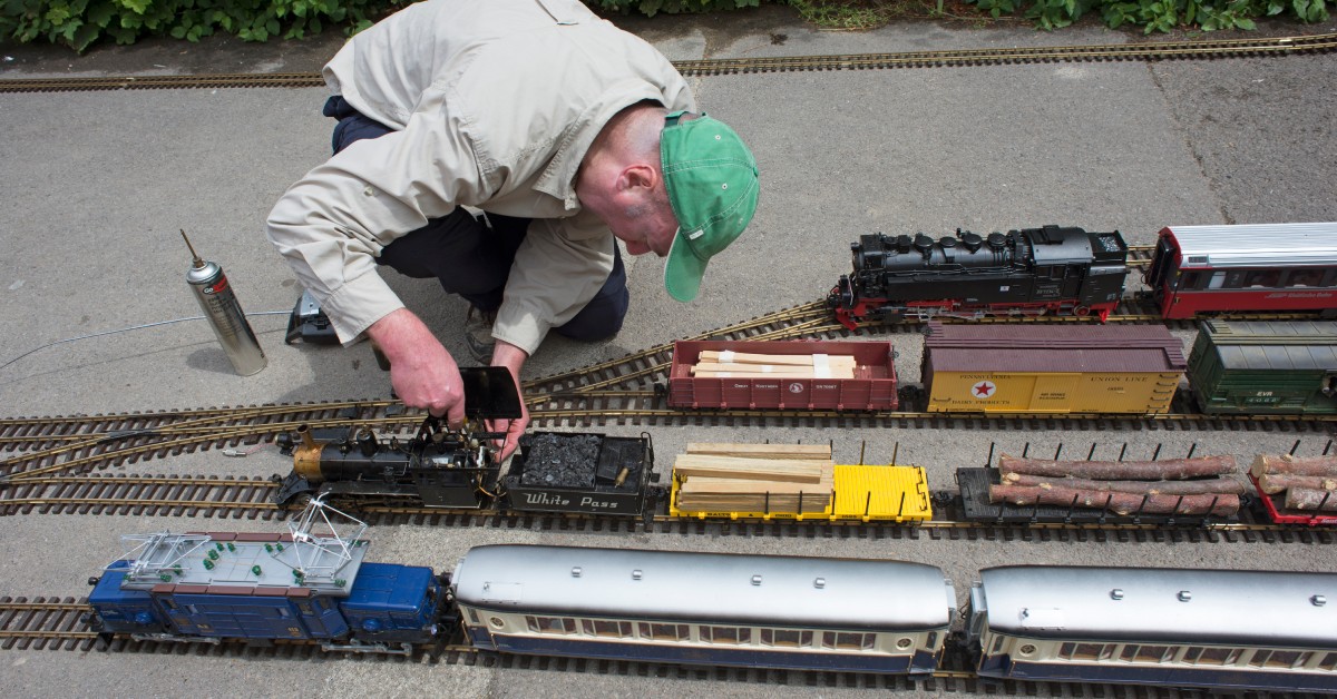A model railway engineer works on his model trains. There are several varieties of trains on the tracks in front of him.