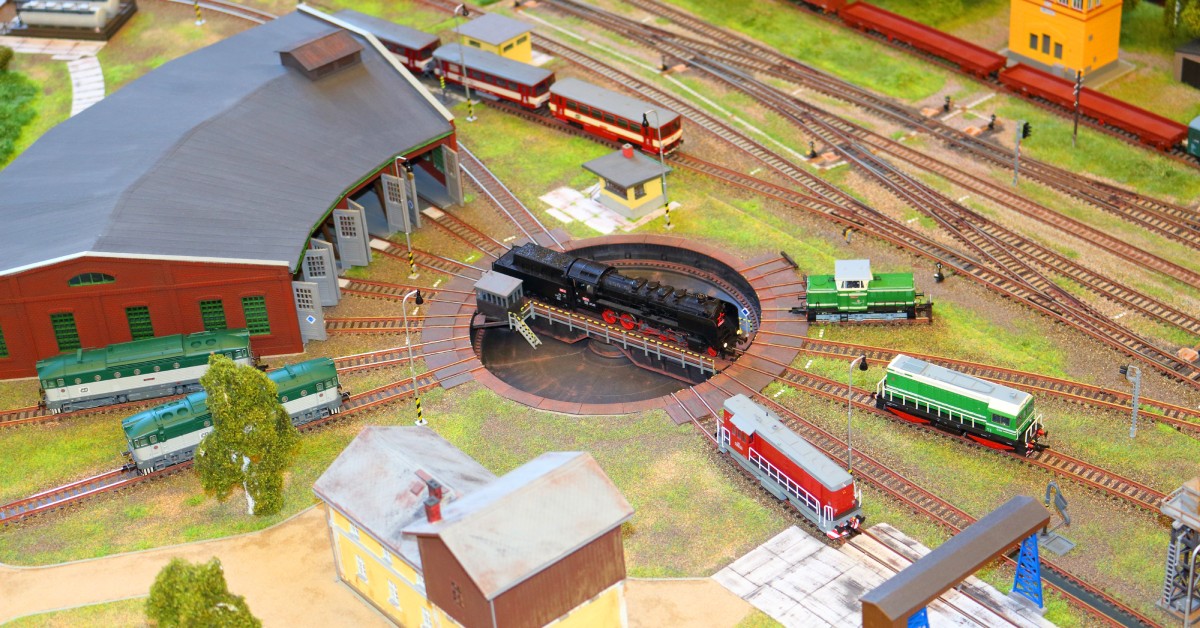 A miniature train set with a rotating piece of machinery in the middle. A black model train is pulling into the depot.