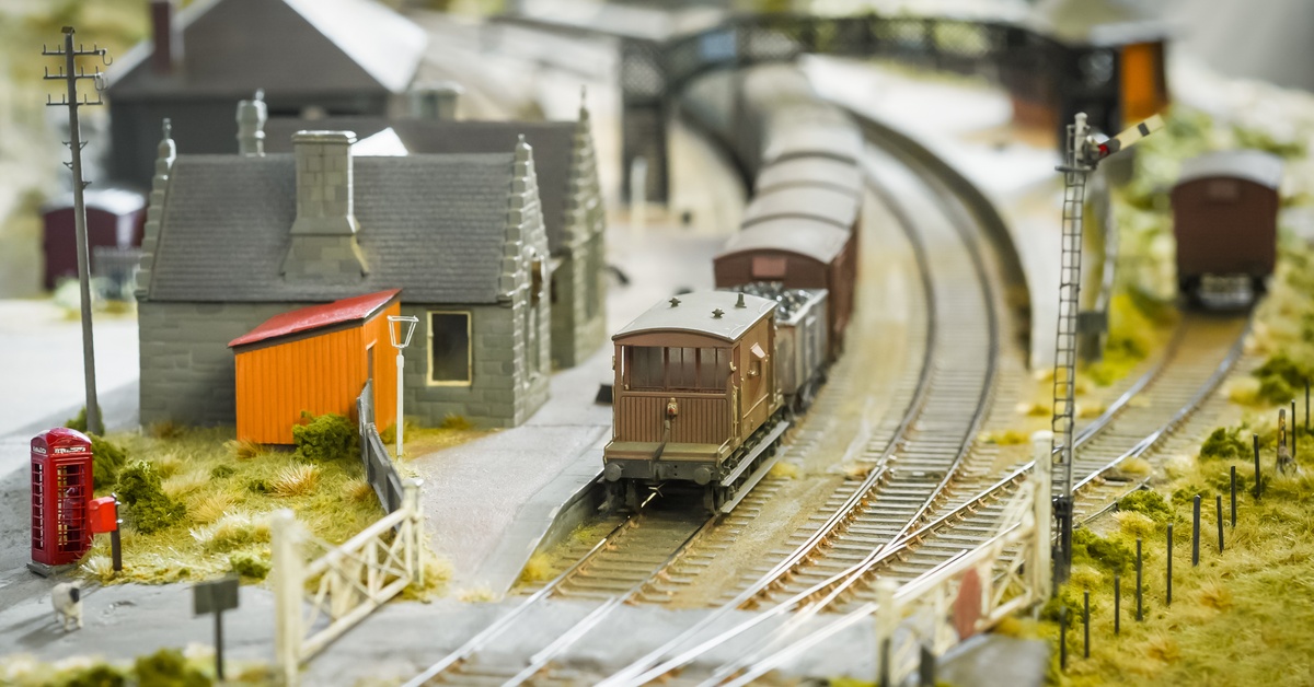 A model trainset set up to look like a rural countryside. A brown train is pulling into a gray train station.