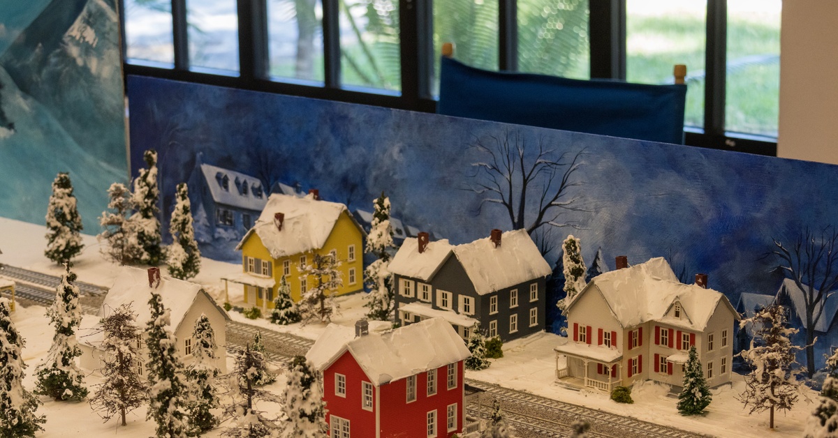 A miniature train set depicting a winter scene. There are multiple multicolored buildings all with snow on their roofs.