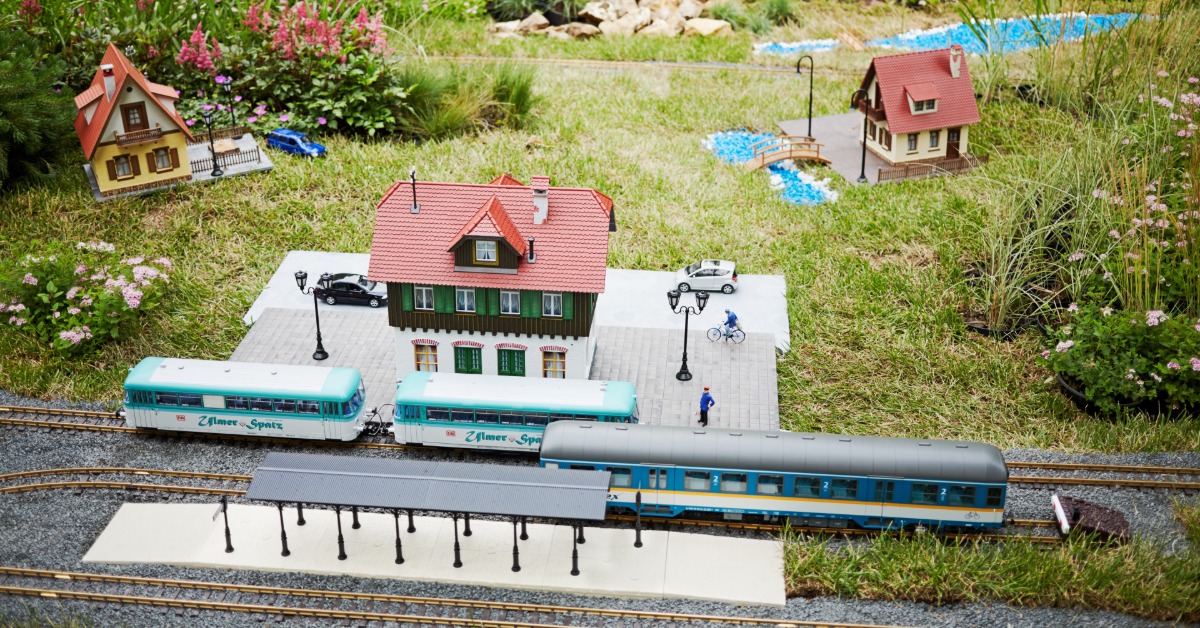 A model train layout in a backyard garden. There are trains on tracks that are next to small bushes and rocks.