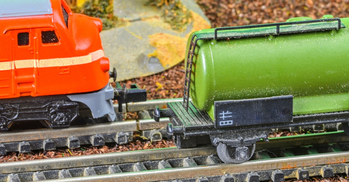 A closeup of a miniature railway with two trains on different tracks. There is a small scale building next to them.