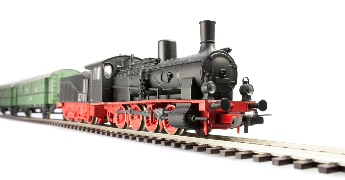 A model of a red and black old steam-powered locomotive train engine pulling green cars against a white background.
