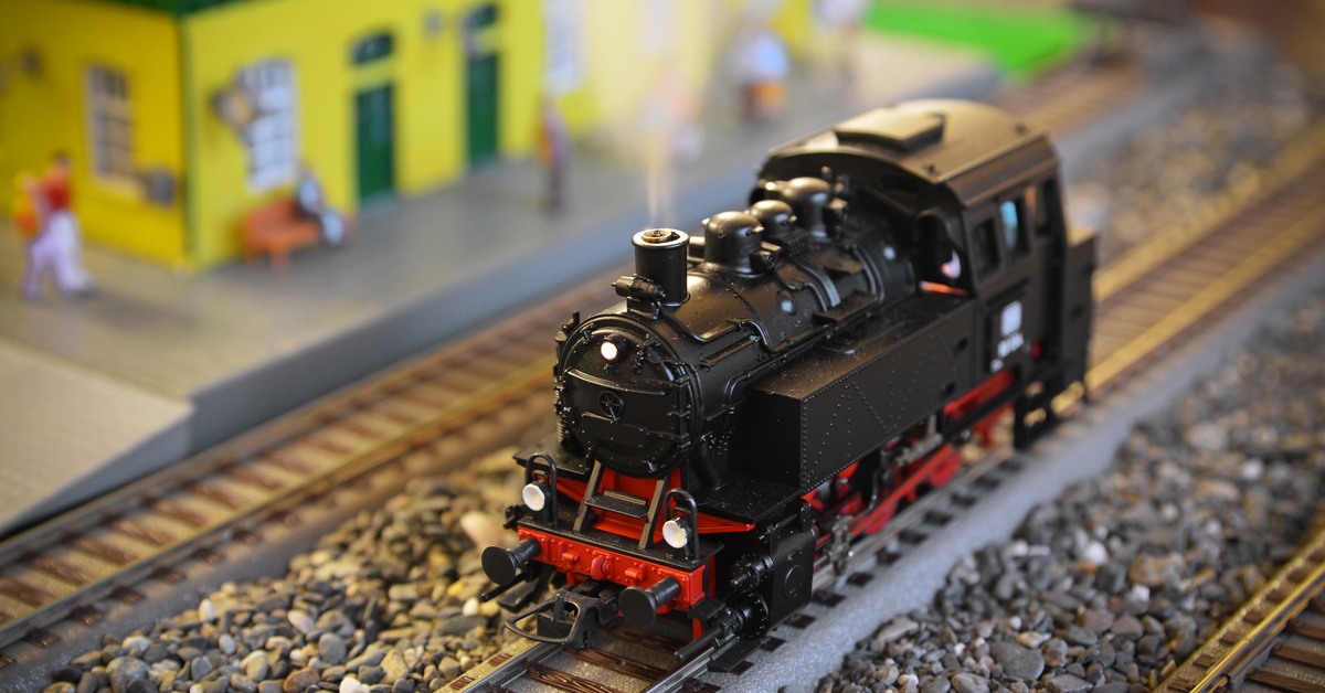 A small model steam locomotive front car sits on the railroad track with smoke coming out of the truck.